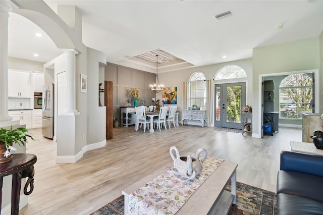 living room featuring a raised ceiling, french doors, light hardwood / wood-style floors, and a notable chandelier