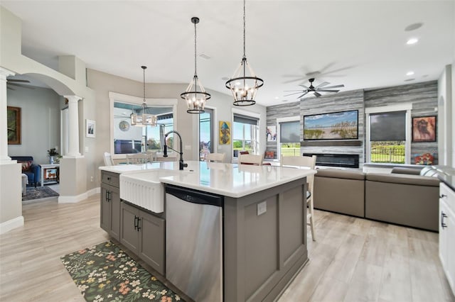 kitchen featuring decorative columns, stainless steel dishwasher, sink, hanging light fixtures, and an island with sink