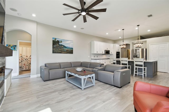 living room featuring ceiling fan with notable chandelier and light hardwood / wood-style flooring