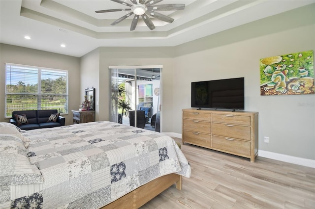 bedroom featuring access to outside, ceiling fan, a tray ceiling, and light hardwood / wood-style floors