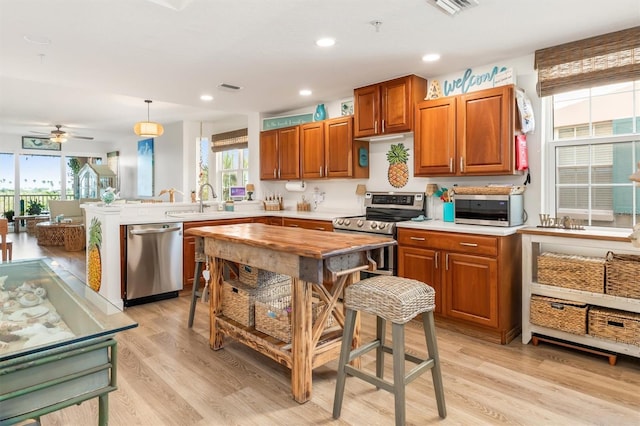 kitchen with kitchen peninsula, appliances with stainless steel finishes, ceiling fan, pendant lighting, and light hardwood / wood-style flooring