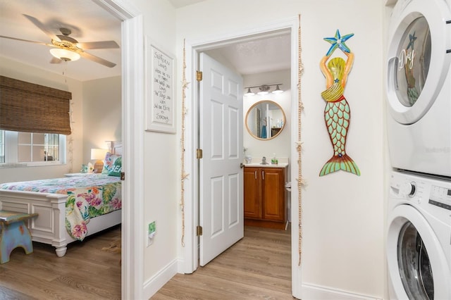 clothes washing area with ceiling fan, stacked washing maching and dryer, and light hardwood / wood-style floors