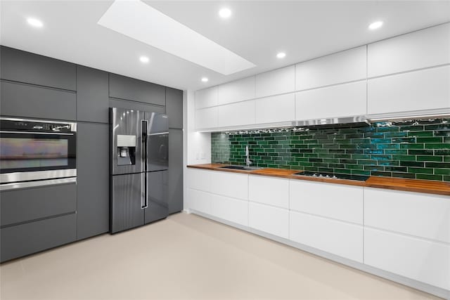 kitchen with appliances with stainless steel finishes, a skylight, butcher block counters, sink, and white cabinets