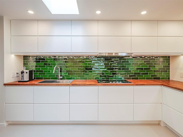 kitchen with wood counters, black stovetop, sink, white cabinets, and backsplash