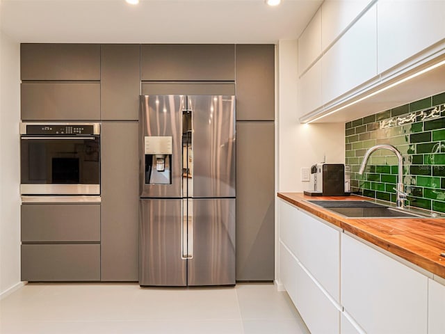 kitchen with wood counters, sink, white cabinets, backsplash, and stainless steel appliances