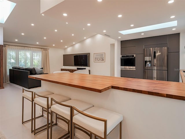 kitchen featuring wood counters, lofted ceiling with skylight, a kitchen breakfast bar, and appliances with stainless steel finishes