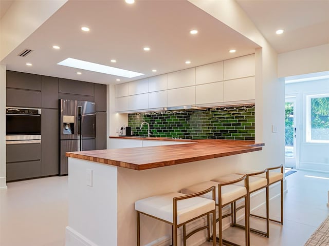 kitchen featuring a breakfast bar, white cabinets, wooden counters, decorative backsplash, and stainless steel refrigerator with ice dispenser