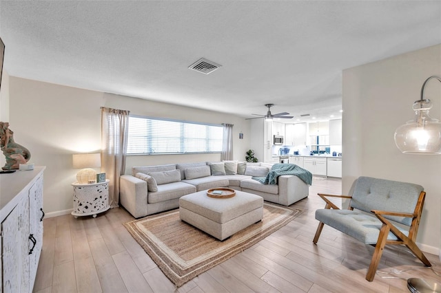 living room featuring a textured ceiling, light hardwood / wood-style floors, and ceiling fan