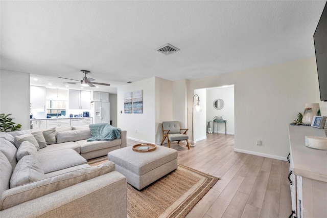 living room featuring a textured ceiling, light hardwood / wood-style flooring, and ceiling fan