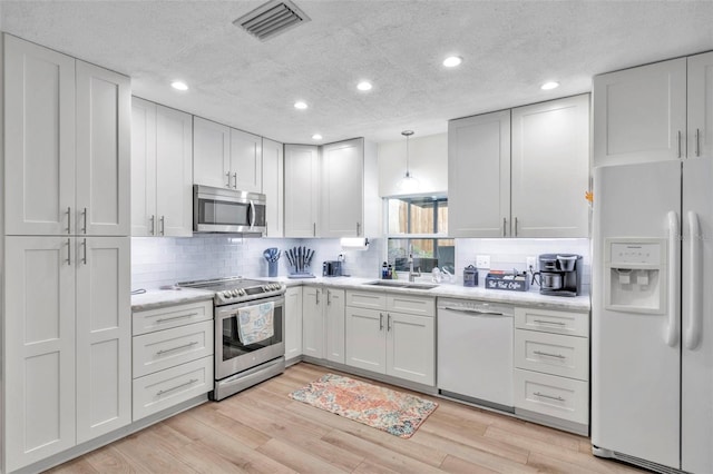 kitchen with sink, appliances with stainless steel finishes, tasteful backsplash, decorative light fixtures, and white cabinetry