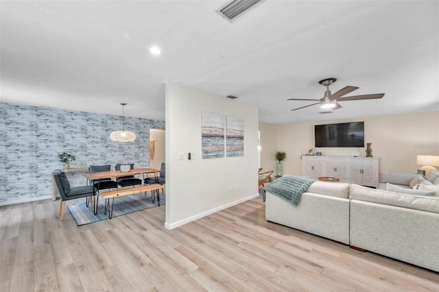 living room featuring ceiling fan, light hardwood / wood-style floors, and a textured ceiling