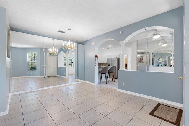 unfurnished dining area featuring decorative columns, light tile patterned flooring, and ceiling fan with notable chandelier