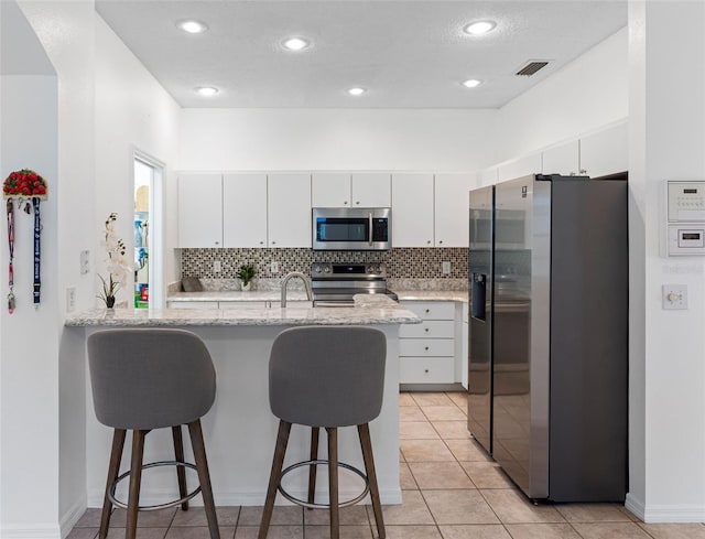 kitchen with light tile patterned flooring, appliances with stainless steel finishes, white cabinets, light stone counters, and kitchen peninsula