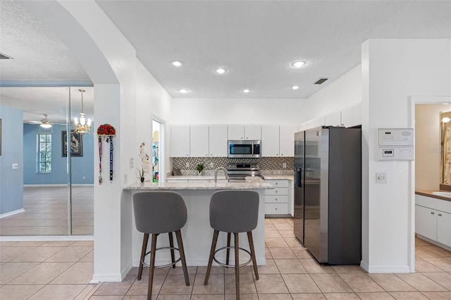 kitchen featuring appliances with stainless steel finishes, white cabinetry, hanging light fixtures, light tile patterned floors, and ceiling fan