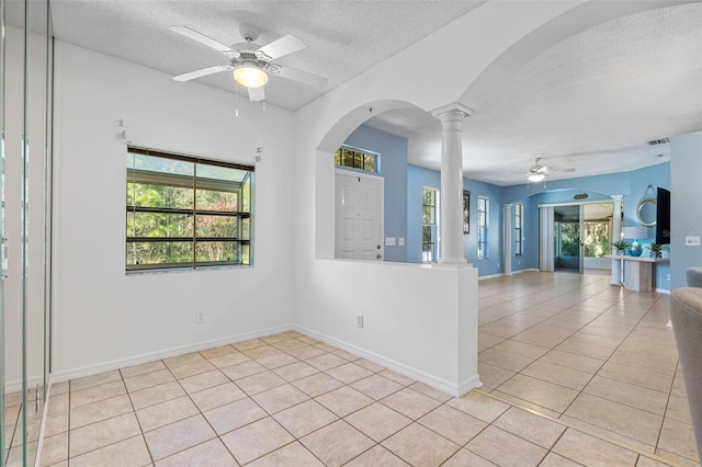 empty room with light tile patterned flooring, ceiling fan, decorative columns, and a textured ceiling