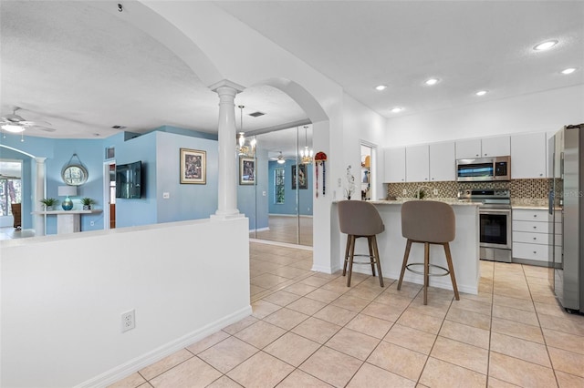 kitchen featuring arched walkways, stainless steel appliances, tasteful backsplash, and ornate columns