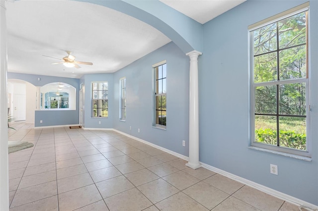 empty room featuring arched walkways, ceiling fan, light tile patterned floors, baseboards, and decorative columns