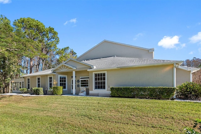 view of front of home with a shingled roof, a front lawn, and stucco siding