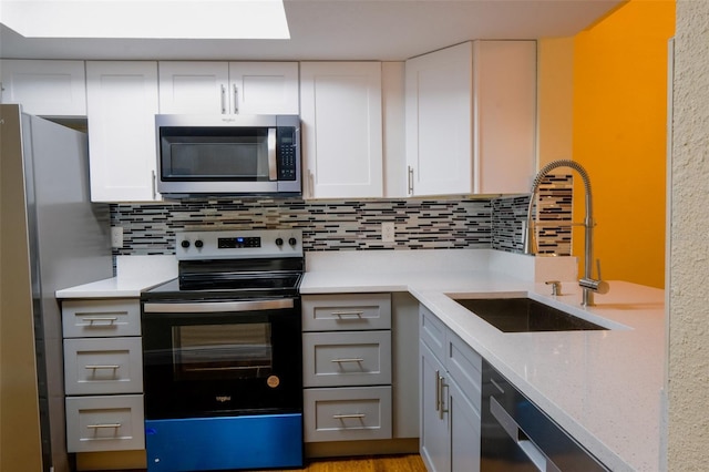 kitchen with sink, light stone counters, backsplash, white cabinets, and appliances with stainless steel finishes