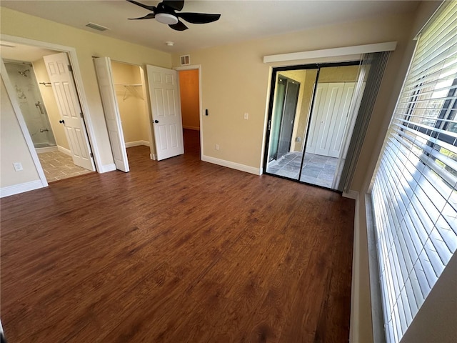 unfurnished bedroom with a barn door, ceiling fan, and dark wood-type flooring