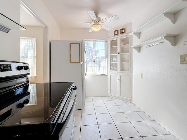 kitchen with stainless steel electric stove, light tile patterned flooring, white cabinets, and range hood