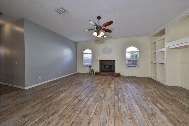 unfurnished living room featuring ceiling fan, wood-type flooring, built in features, and a tiled fireplace