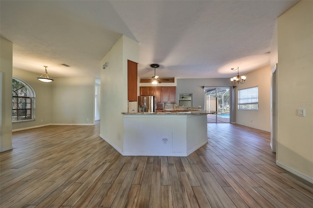 kitchen with kitchen peninsula, stainless steel refrigerator with ice dispenser, light wood-type flooring, and ceiling fan with notable chandelier