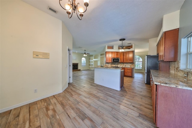 kitchen featuring light wood-type flooring, stainless steel appliances, hanging light fixtures, and backsplash