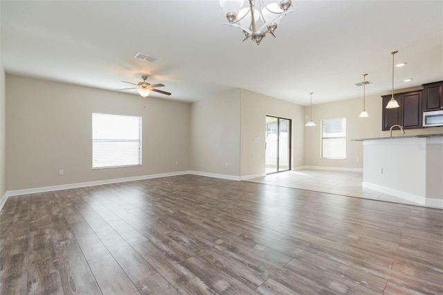 unfurnished living room with ceiling fan with notable chandelier and light hardwood / wood-style flooring