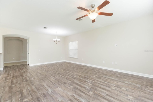 empty room with ceiling fan with notable chandelier and light hardwood / wood-style floors