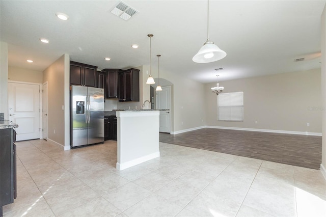 kitchen with stainless steel refrigerator with ice dispenser, dark brown cabinetry, light stone counters, and pendant lighting