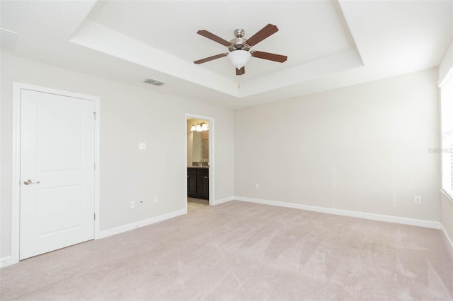 unfurnished room with ceiling fan, a raised ceiling, and light carpet