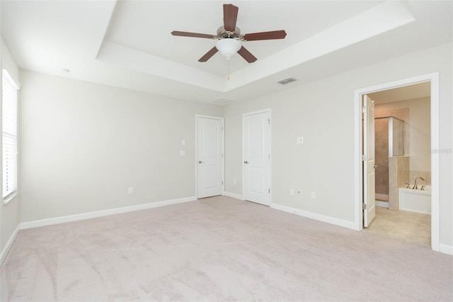 unfurnished bedroom featuring ensuite bath, ceiling fan, light carpet, and a tray ceiling