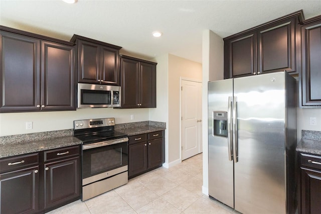 kitchen featuring appliances with stainless steel finishes, light tile patterned floors, dark brown cabinets, and dark stone countertops