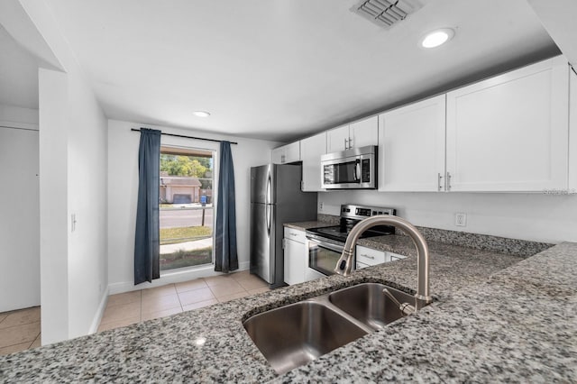 kitchen featuring appliances with stainless steel finishes, dark stone counters, sink, light tile patterned floors, and white cabinetry