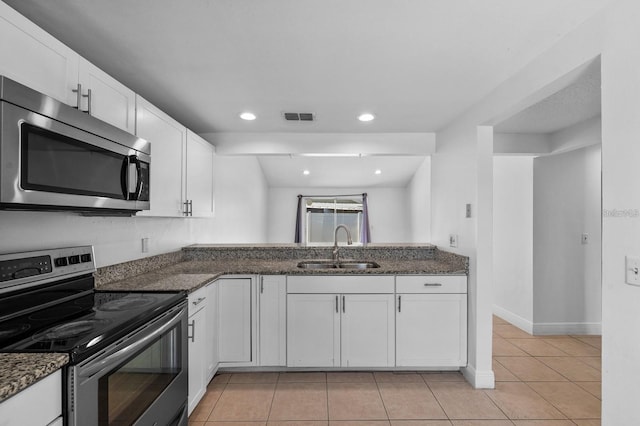 kitchen with dark stone counters, white cabinets, sink, light tile patterned floors, and stainless steel appliances