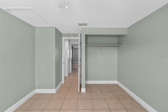 unfurnished bedroom featuring light tile patterned floors, a textured ceiling, a closet, and ceiling fan