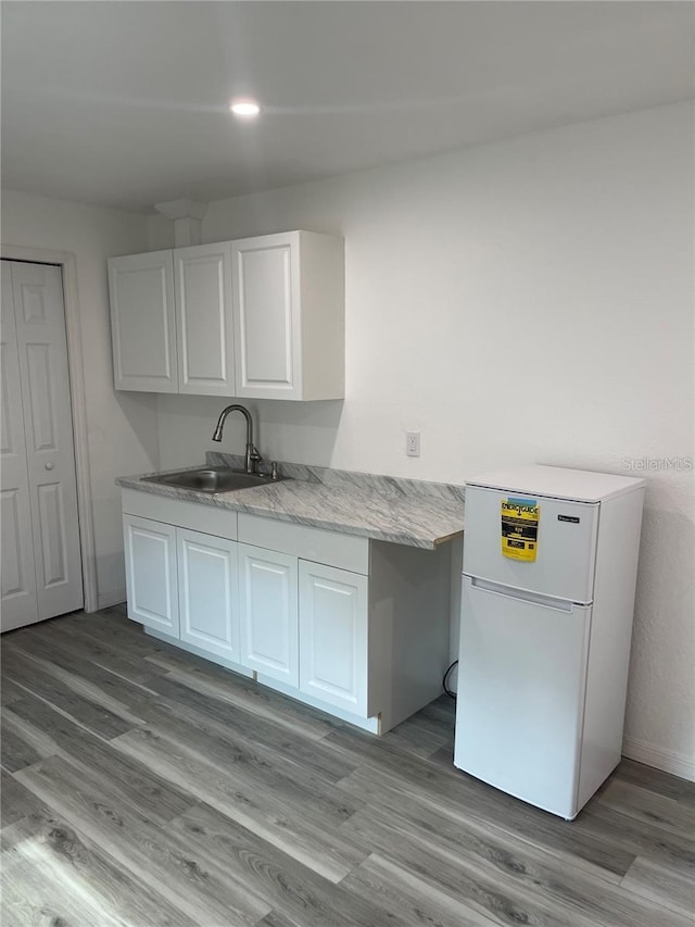 kitchen with white cabinets, white refrigerator, light hardwood / wood-style floors, and sink