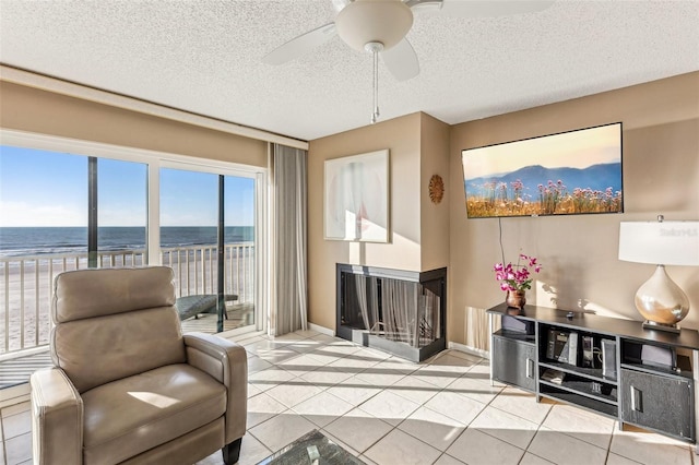 sitting room with a textured ceiling, a multi sided fireplace, a water view, ceiling fan, and light tile patterned floors