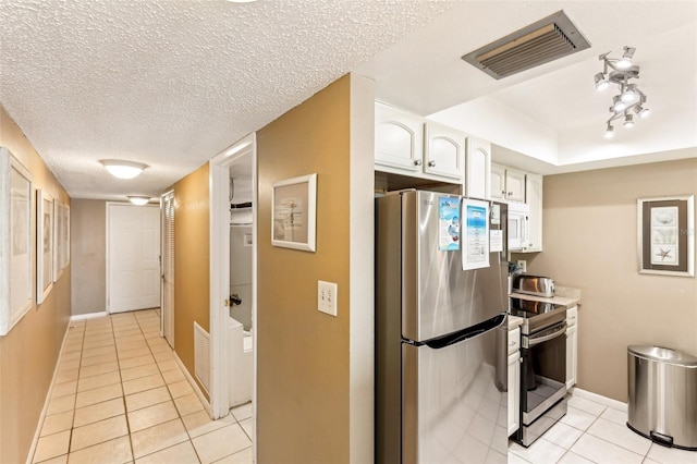 kitchen with a textured ceiling, light tile patterned floors, stainless steel appliances, and white cabinetry