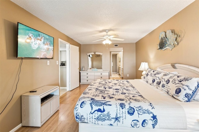 bedroom featuring ceiling fan, light wood-type flooring, ensuite bathroom, and a textured ceiling