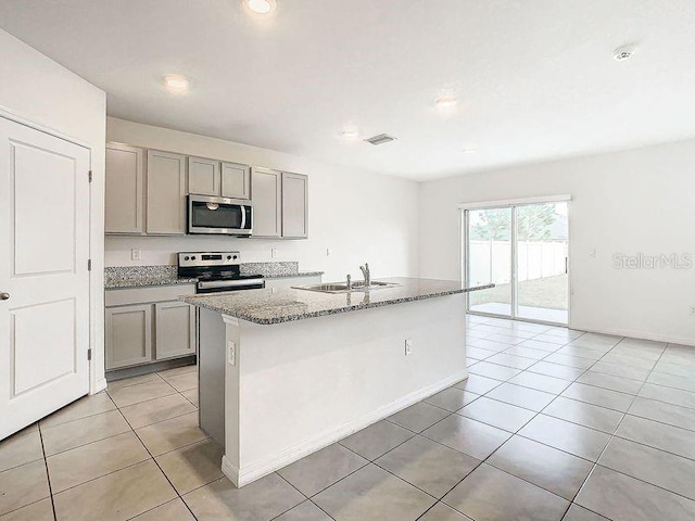 kitchen with sink, a center island with sink, light stone counters, and appliances with stainless steel finishes