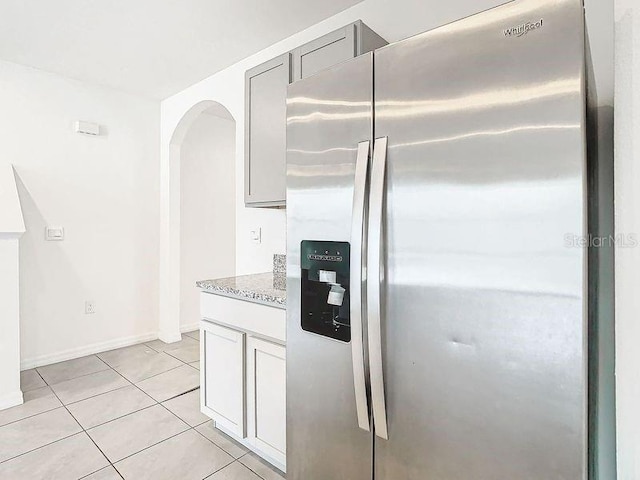 kitchen with gray cabinetry, stainless steel fridge with ice dispenser, light tile patterned floors, and stone countertops