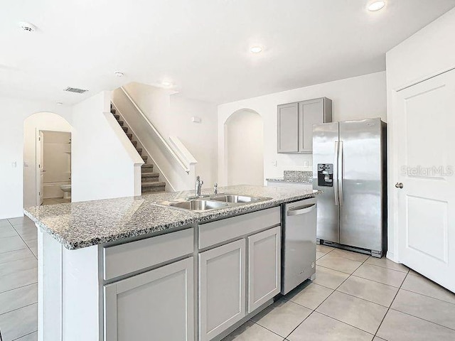 kitchen with sink, gray cabinets, an island with sink, appliances with stainless steel finishes, and light tile patterned flooring