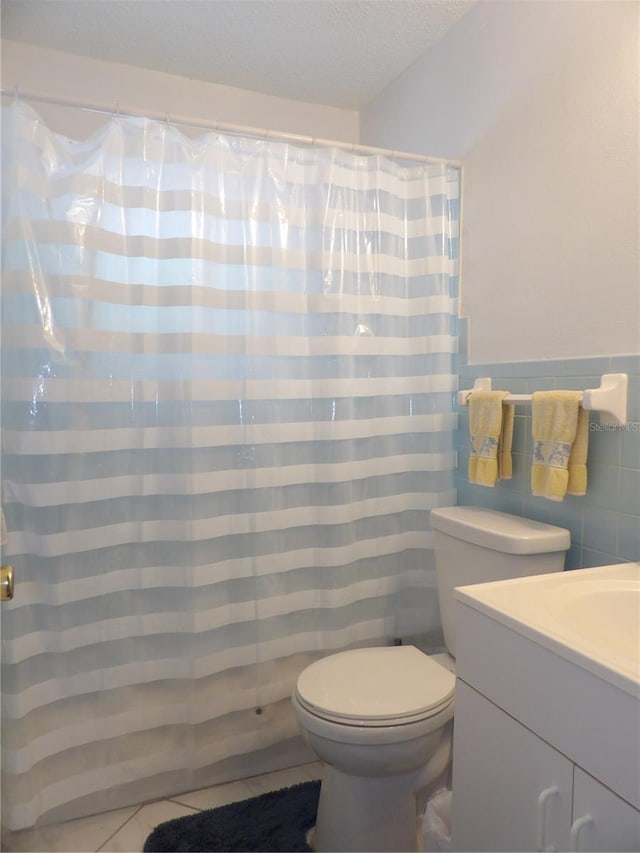 bathroom with toilet, a textured ceiling, walk in shower, tile walls, and vanity