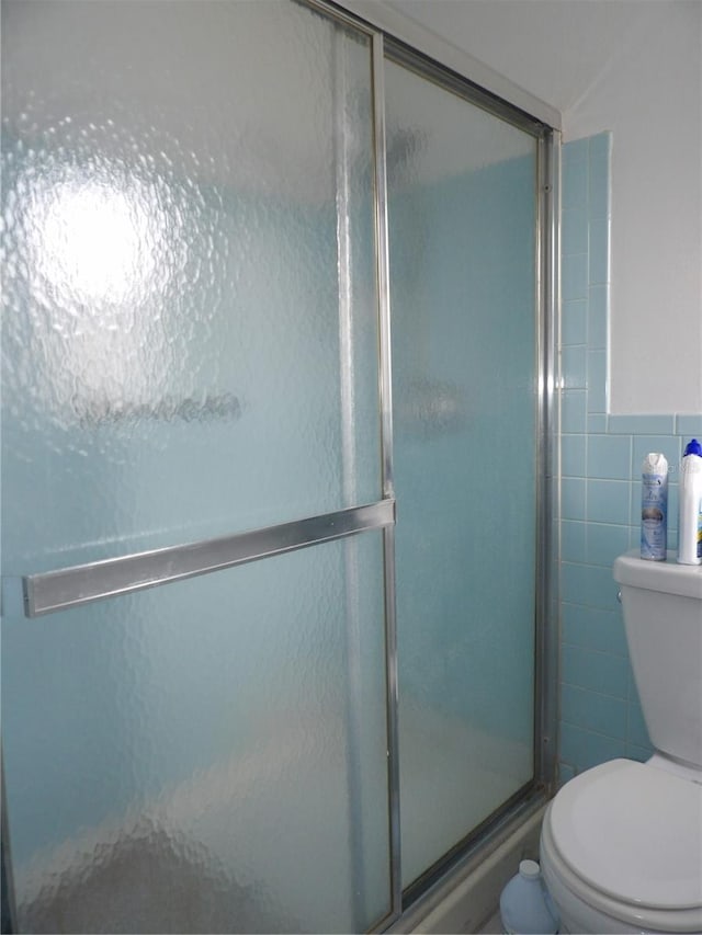 bathroom featuring toilet, a shower with shower door, and tile walls