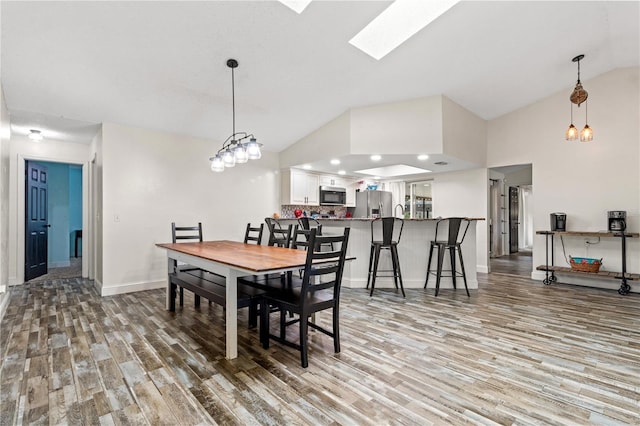 dining space featuring wood-type flooring and vaulted ceiling with skylight