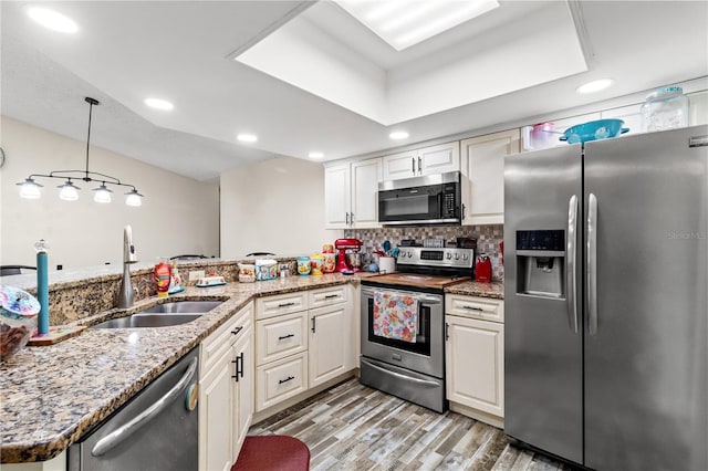 kitchen featuring pendant lighting, sink, stainless steel appliances, kitchen peninsula, and light wood-type flooring