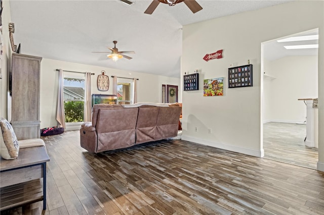 living room featuring dark hardwood / wood-style floors, ceiling fan, vaulted ceiling with skylight, and a textured ceiling