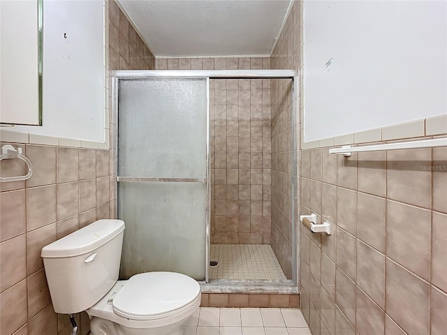 bathroom with tile patterned floors, an enclosed shower, a textured ceiling, toilet, and tile walls